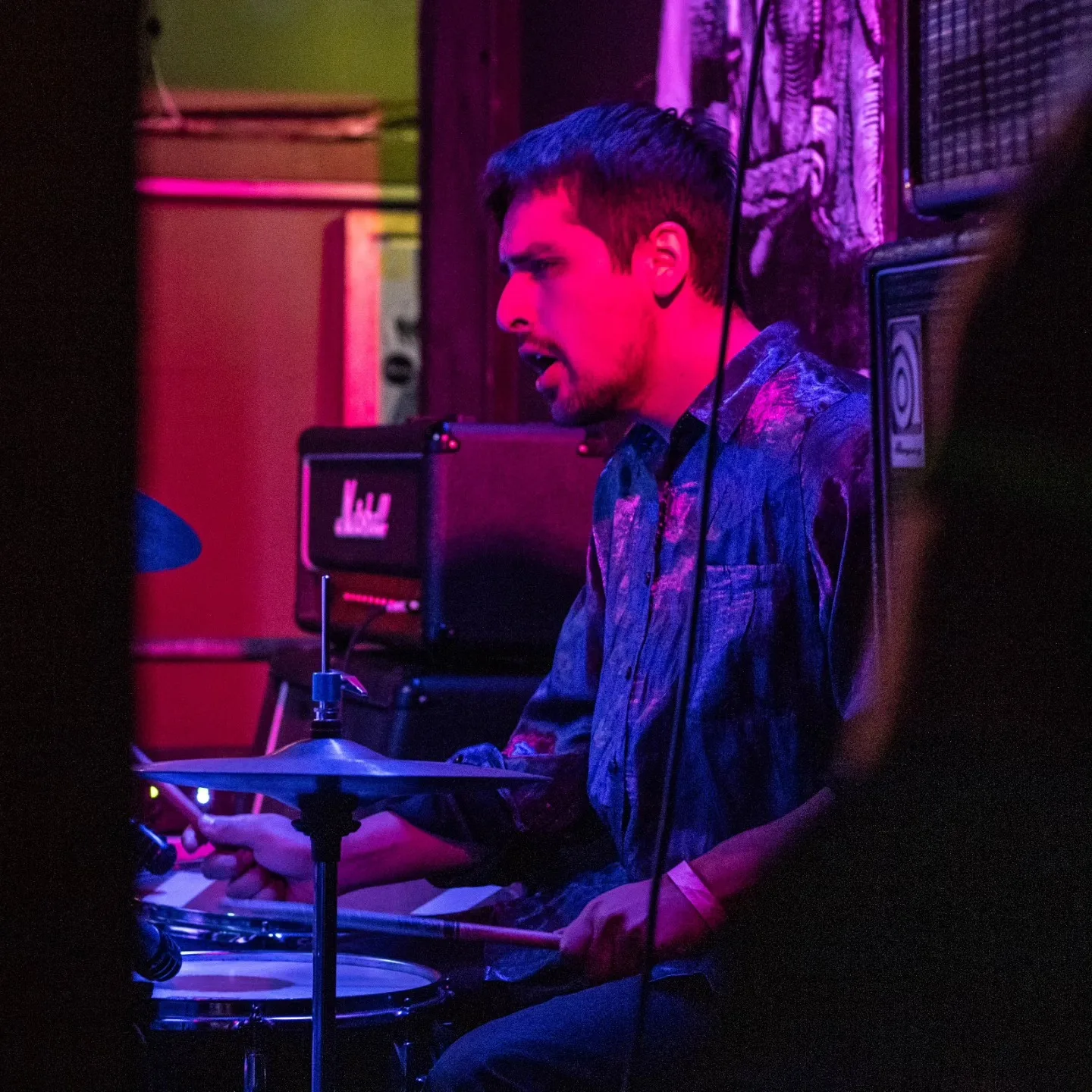 Baterista de Phuyu y la Fantasma tocando bajo luz magenta y azul